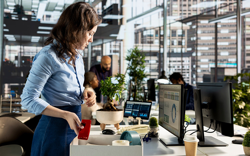Una lavoratrice che impacchetta oggetti in una scatola in un ufficio moderno, simboleggiando il trasferimento del lavoratore.