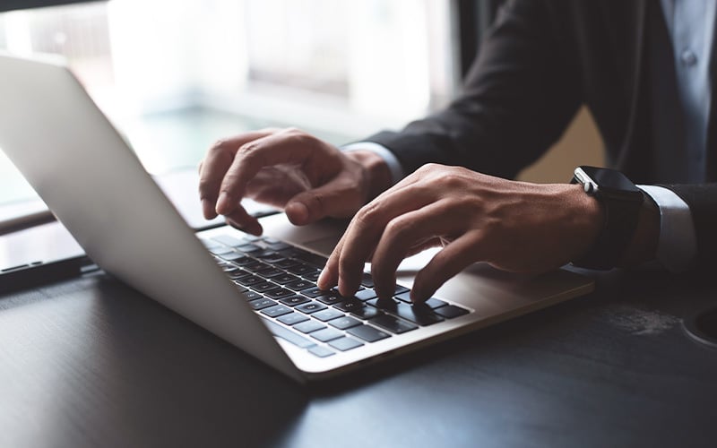 Un uomo d'affari che digita velocemente su un laptop con uno smart-watch al polso, in riferimento alla compilazione digitale del Modello UNILAV